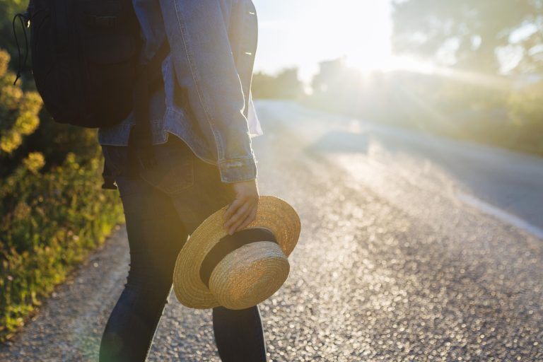 side view woman with backpack road holding hat